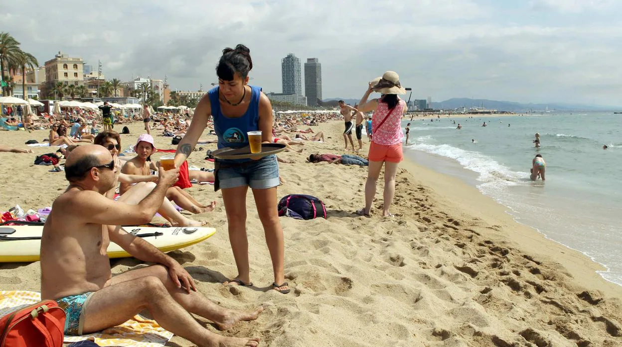 Una camarera de un chiringuito de la playa de la Barceloneta sirve una cerveza en la orilla