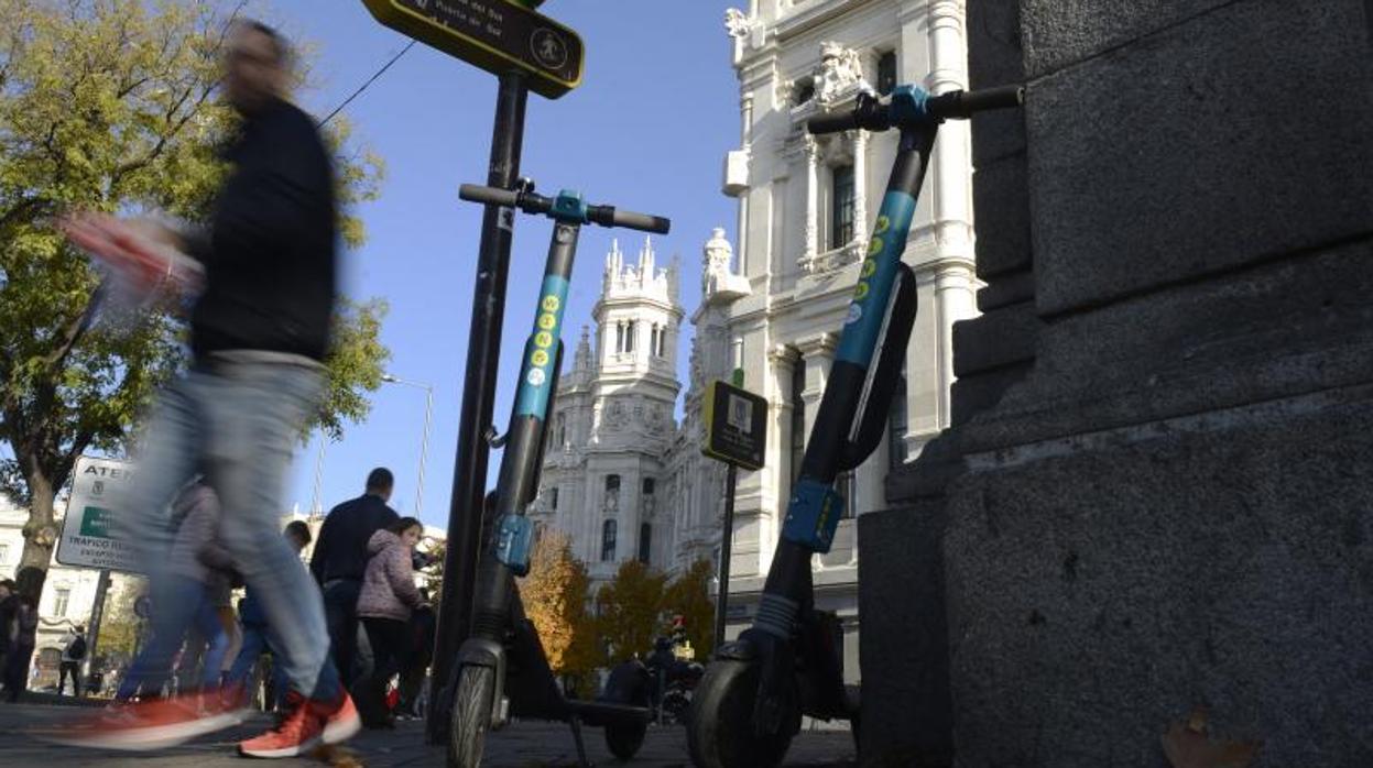 Dos patinetes apoyados en una acera junto al Palacio de Cibeles