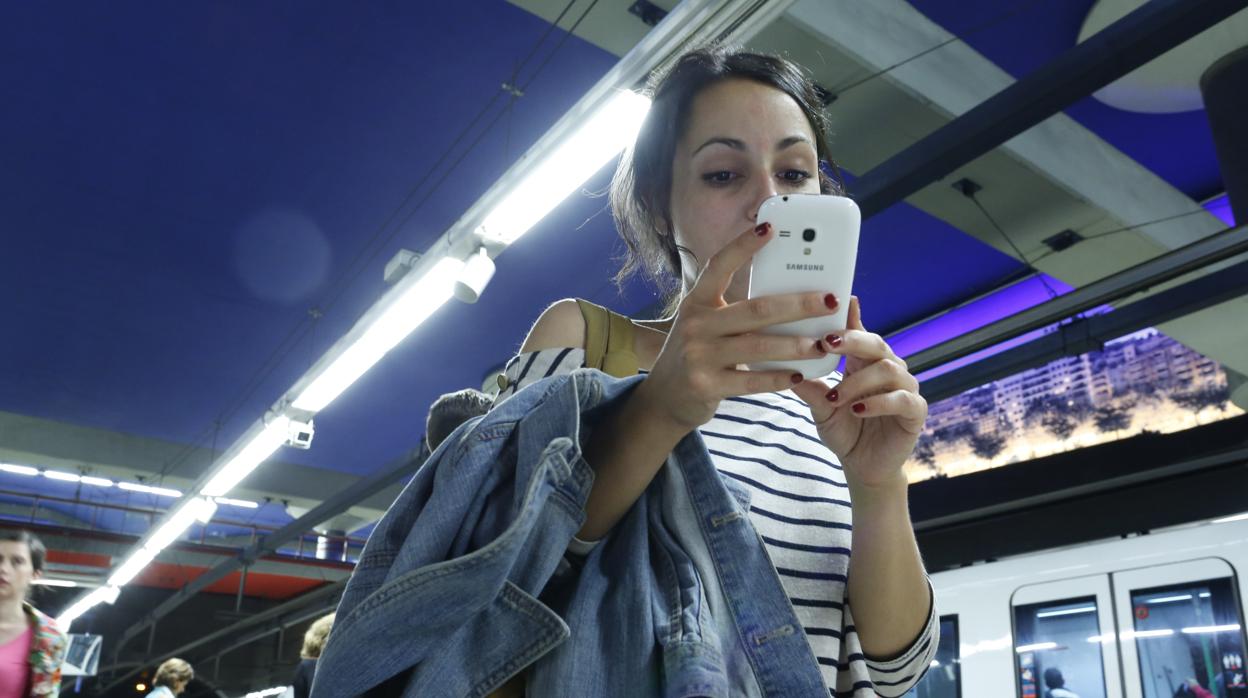 Una joven consulta su teléfono móvil en un andén del metro