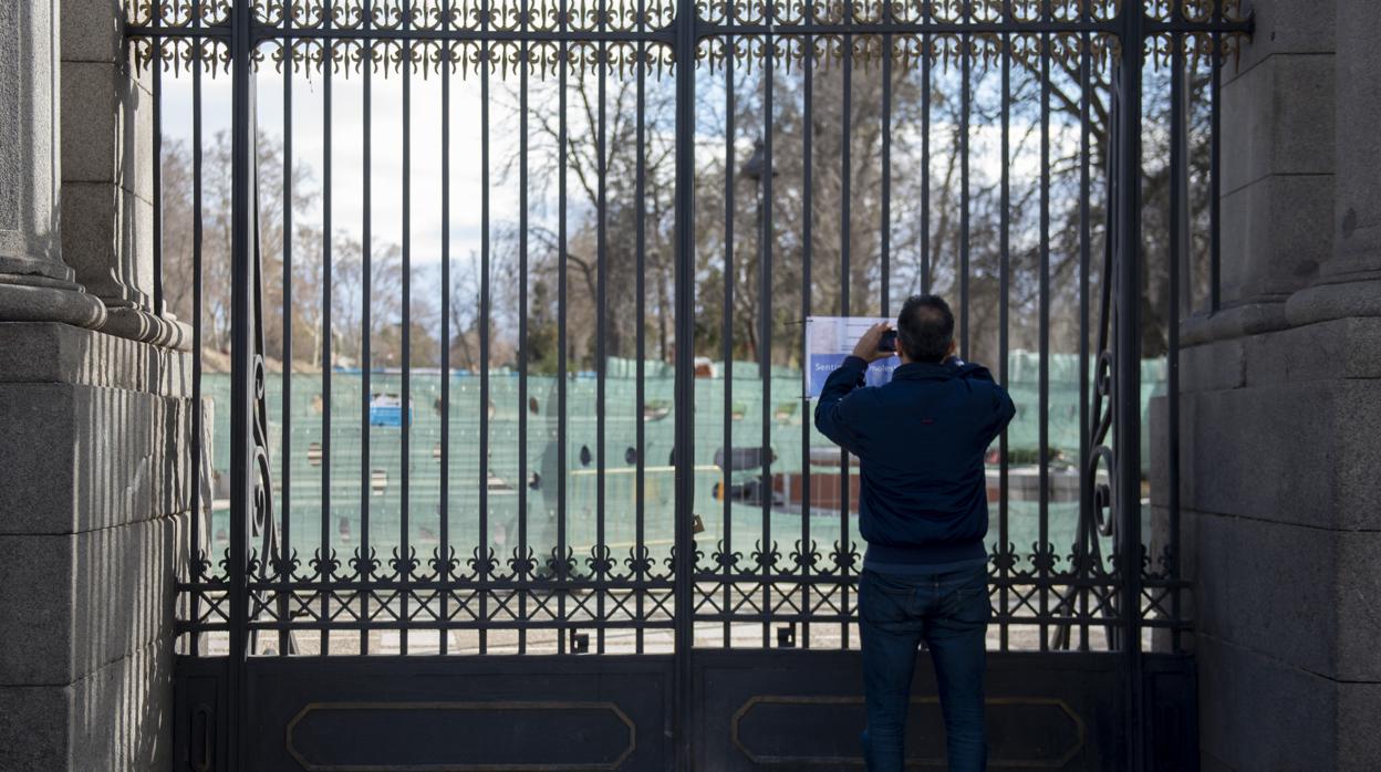 Un ciudadano realiza una foto a un cartel que informa del cierre temporal de El Retiro