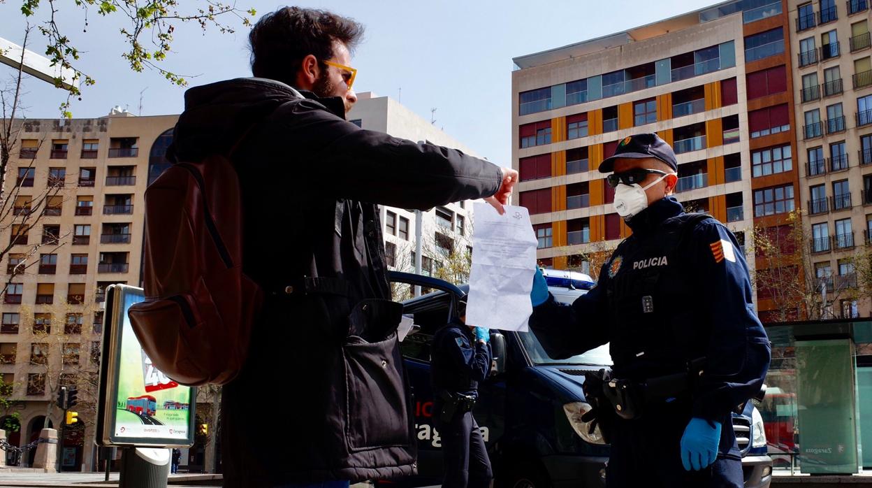 Un policía nacional revisa el documento con el que un ciudadano acredita el motivo por el que ha tenido que salir a la calle, en un control establecido en el centro de Zaragoza