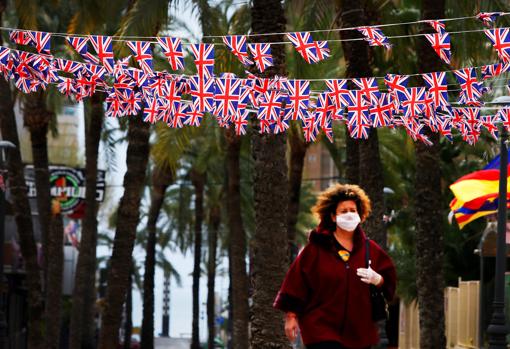 Una turista con máscara pasa por debajo de banderas británicas colgadas en una de las calles de la zona inglesa de Benidorm