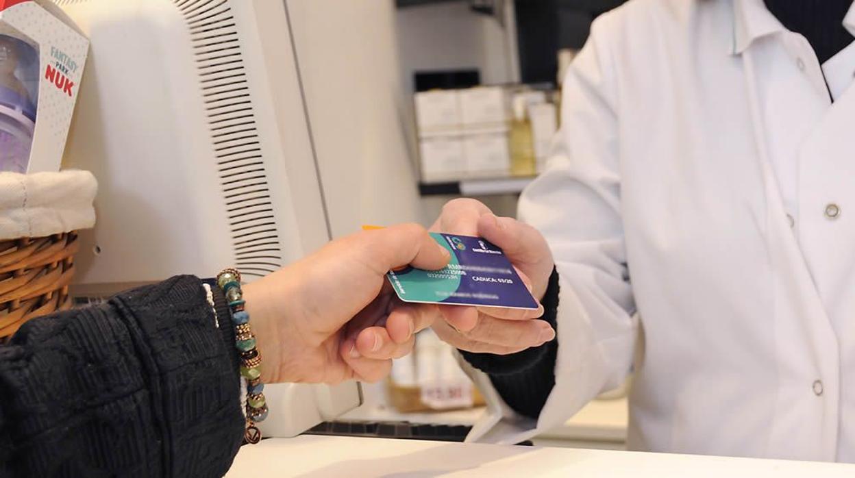 Un ciudadano muestra su tarjeta sanitaria en una farmacia