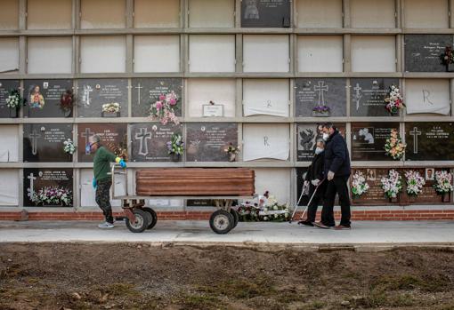 Un operario de un cementerio de ValEncia traslada un féretro seguido por los familiares de la víctima durante un entierro, que a causa del coronavirus, se tienen que realizar con el nuevo protocolo de seguridad