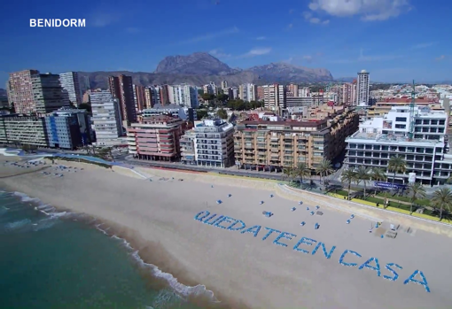 La playa de Benidorm con el lema «Quédate en casa» escrito con hamacas sobre la arena