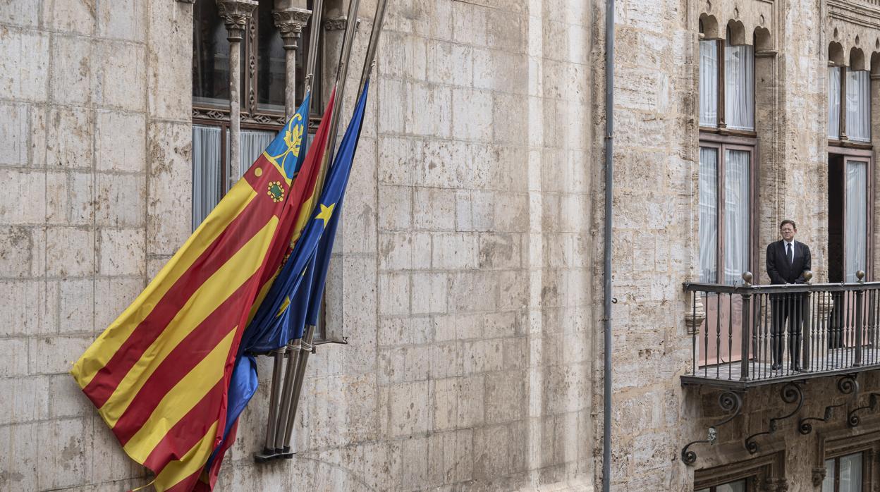 El presidente de la Generalitat, Ximo Puig, guarda tres minutos de silencio desde el balcón del Palau de la Generalitat con las banderas a media asta