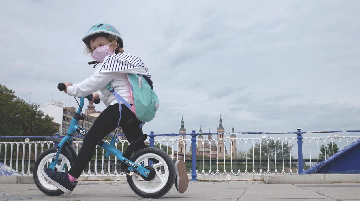 Una niña con mascarilla pasea en bicicleta en Zaragoza, con la Basílica del Pilar al fondo