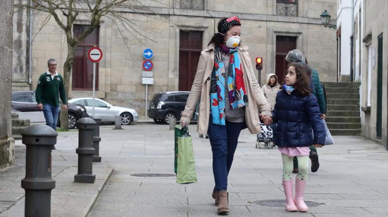 Una mujer, protegida con una mascarilla, camina con una menor por una calle de Santiago