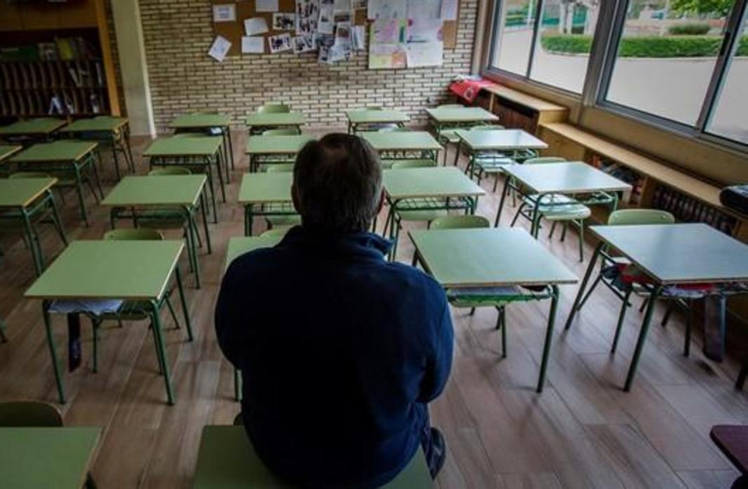 Un profesor, delante de las mesas vacías en el aula que da clase