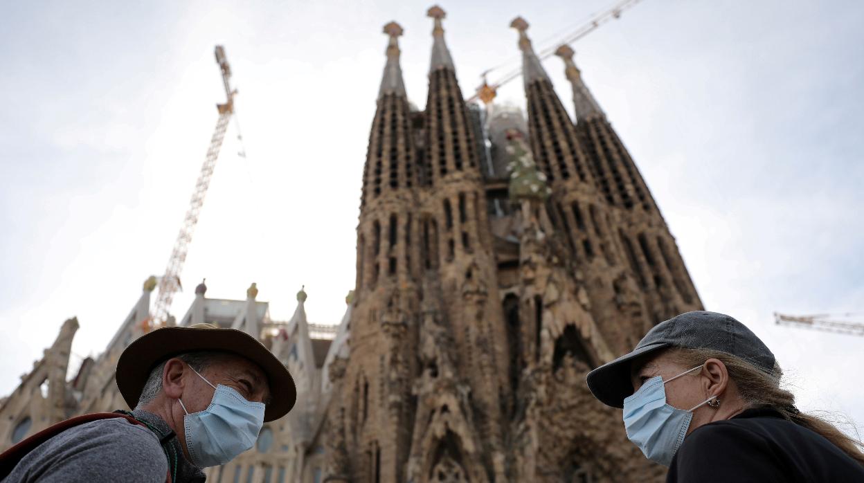 Dos personas con mascarilla, fotografiados ante la Sagrada Familia