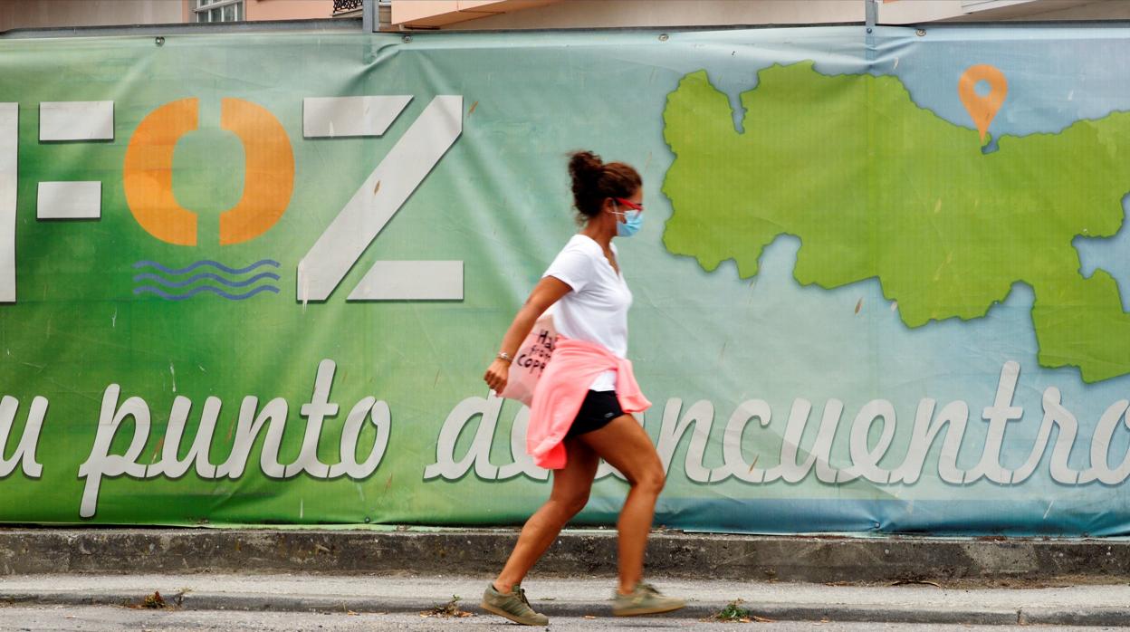 Una mujer con mascarilla camina frente a un cartel publicitario en Foz