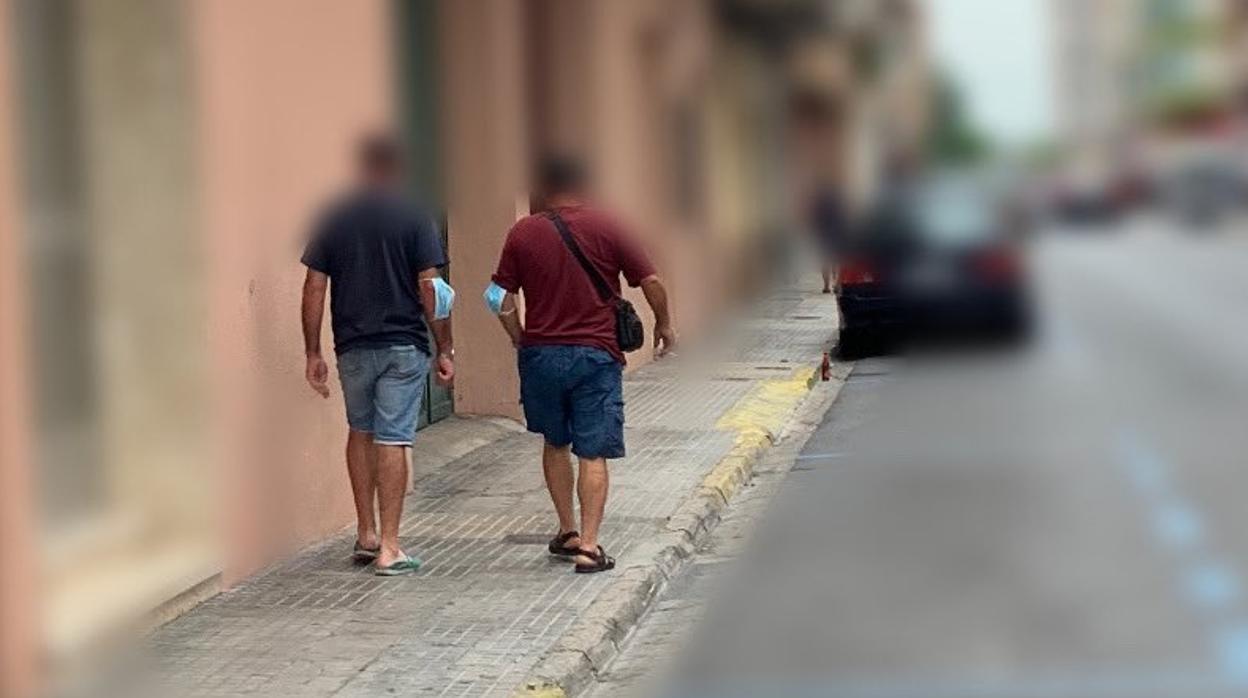 Imagen de dos personas paseando por la calle con la mascarilla en el codo