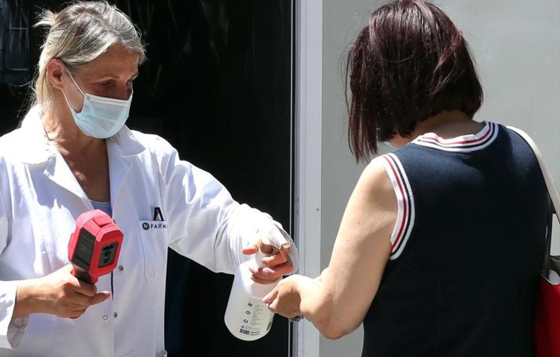 Una mujer desinfecta a otra con gel hidroalcohólico y le toma la temperatura