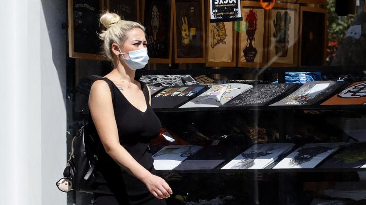 Una mujer pasea por Alicante con mascarilla en una zona de comercios