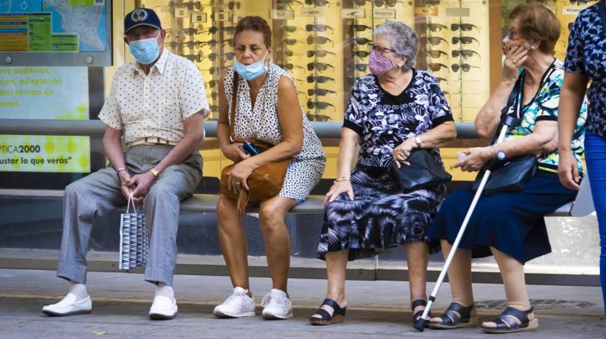 Varios ancianos con mascarilla sentados en un banco en una calle de Alicante