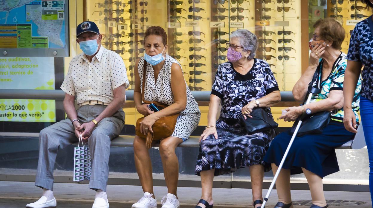 Imagen de archivo de personas con mascarilla en una parada de autobús en Alicante