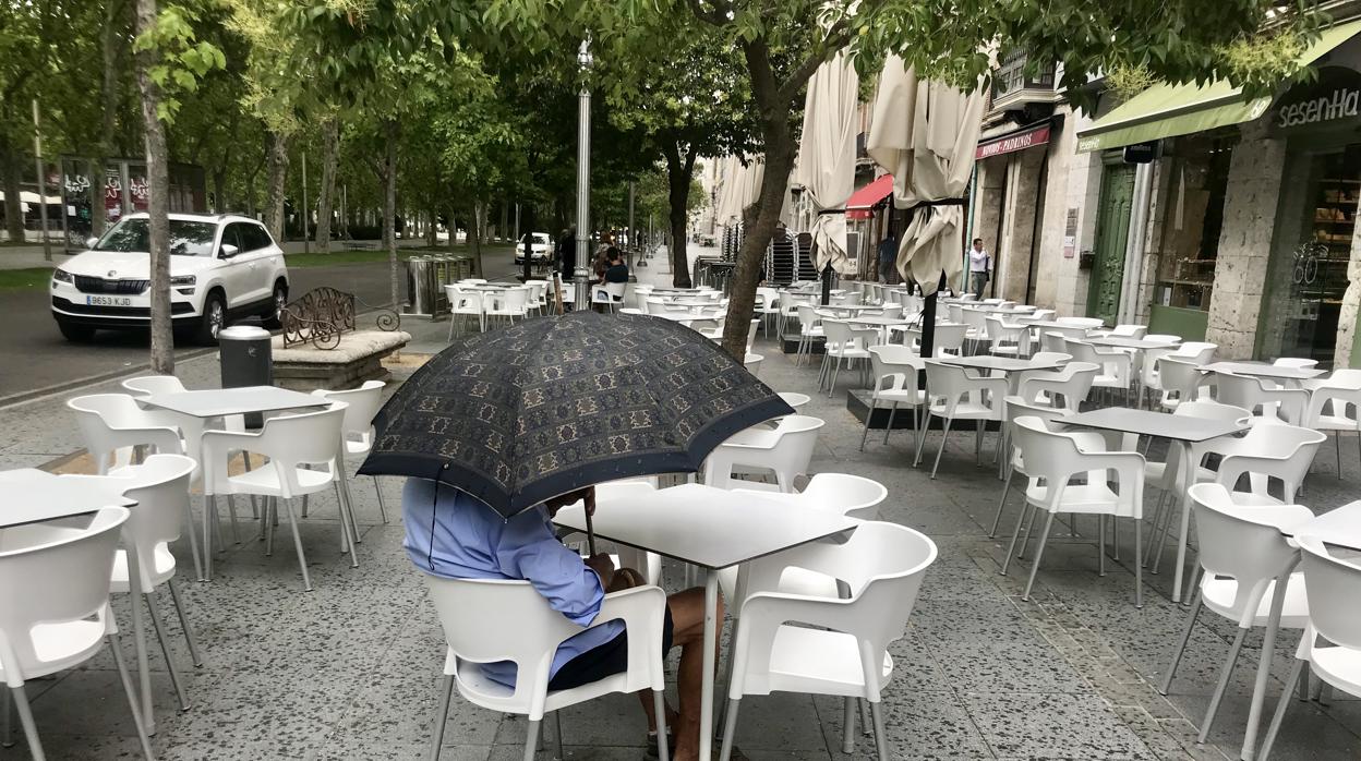 Un hombre se resguarda de la lluvia en una terraza vacía, en Valladolid