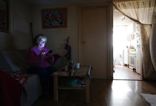 Mª Ángeles mira el móvil en su piso, sin apenas luz natural