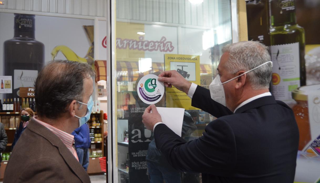 El presidente de la Diputación de Guadalajara, José Luis Vega, y el presidente de la Asociación Provincial de Agricultores y Ganaderos (Apag), Juan José Laso, pegan el distintivo especial de «Alimentos de Guadalajara»