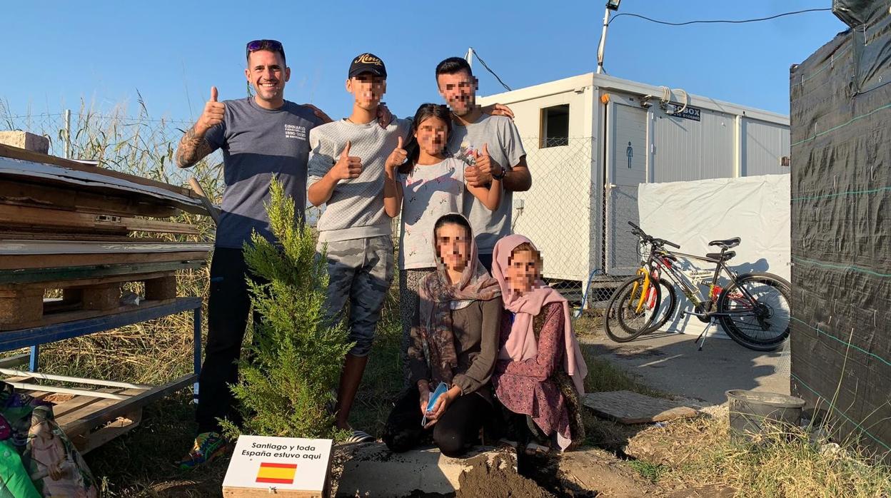 Santiago Sánchez, junto a varios refugiados y un árbol plantado en el campo de Nea Kavala