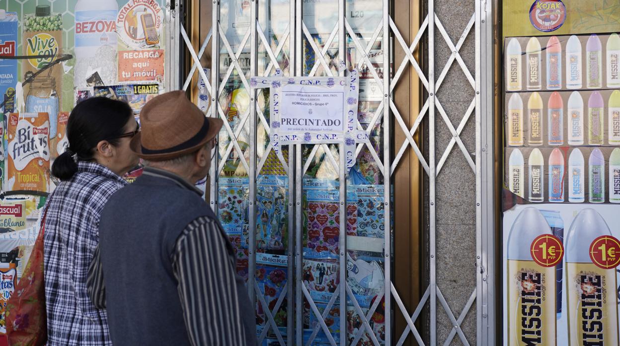 Dos vecinos de Vicálvaro leen el precinto policial en la puerta de la tienda de Paquito tras su asesinato