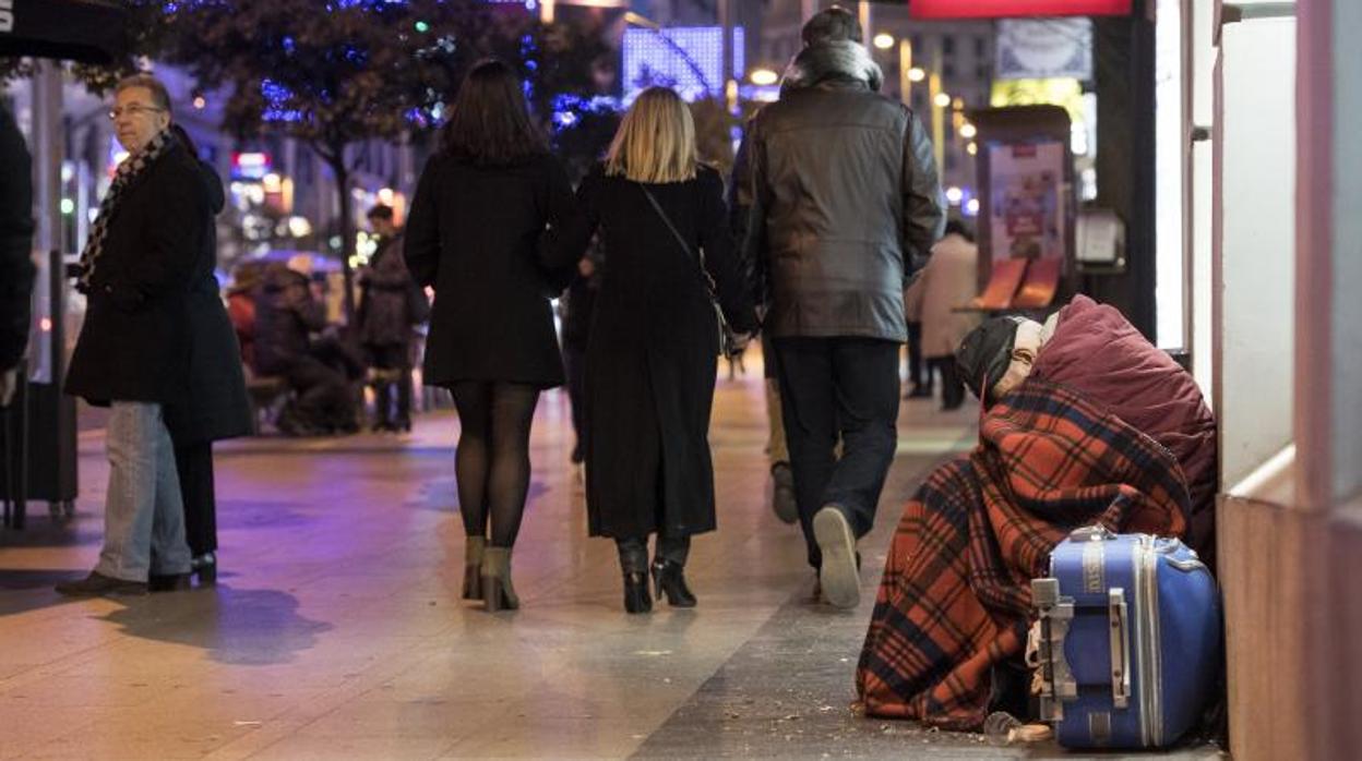 Un hombre sin hogar se arropa con una manta en una céntrica calle de Madrid