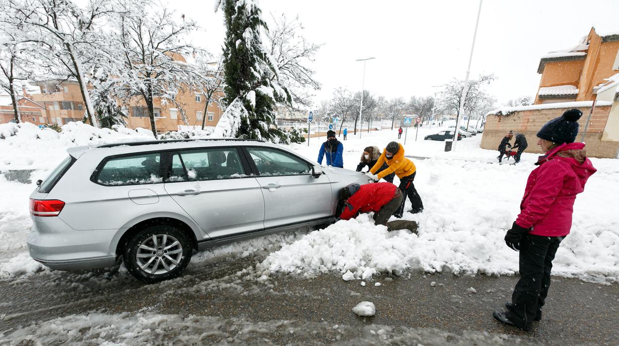 Varias personas ayudan a un conductor de un vehículo atascado en la urbanización La Legua por la nieve