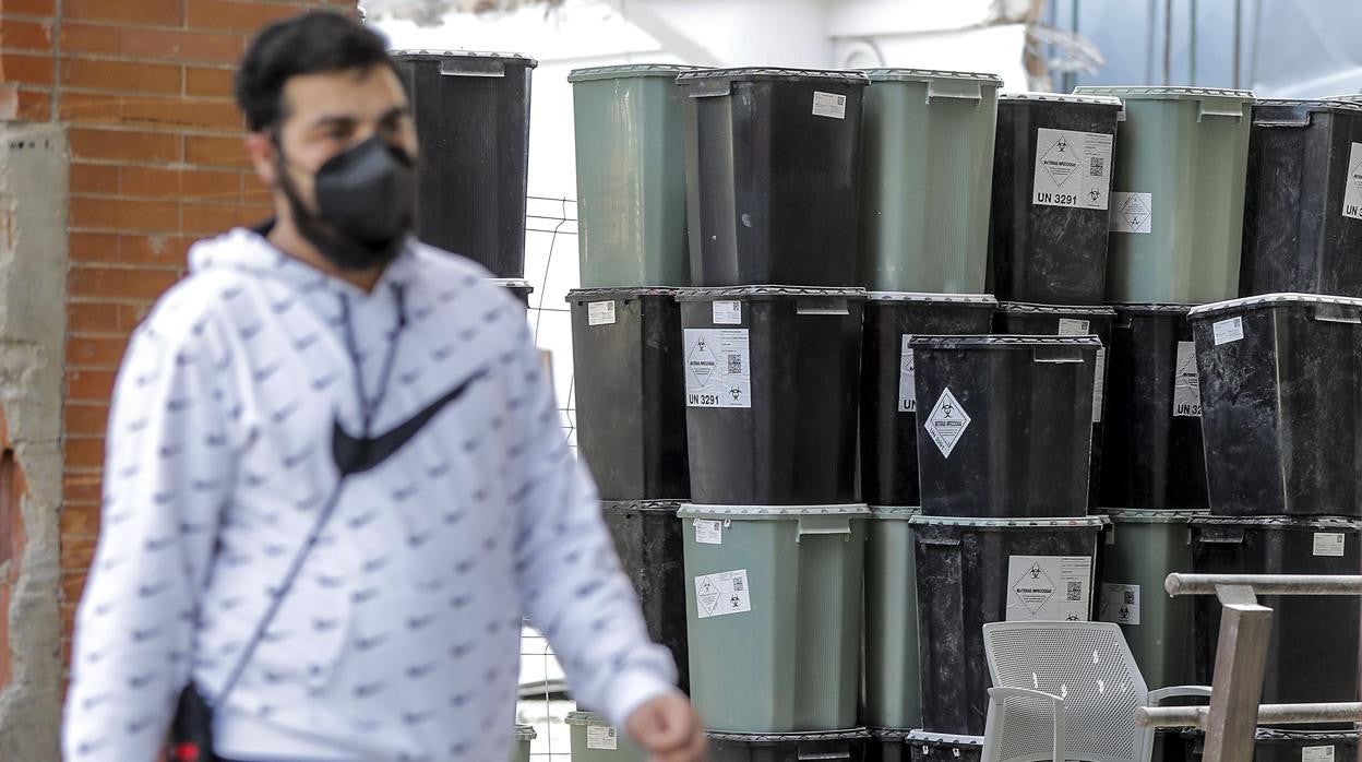 Imagen de un viandante pasando junto a los contenedores apilados en el exterior del Hospital Clínico de Valencia