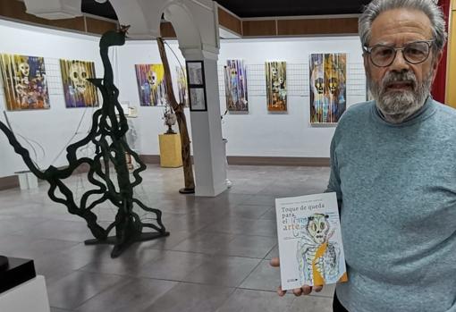 Los cuadros están colgados en su sala de exposiciones de Pedro Muñoz. El pintor sostiene un ejemplar del libro de Gregorio Vigil-Escalera