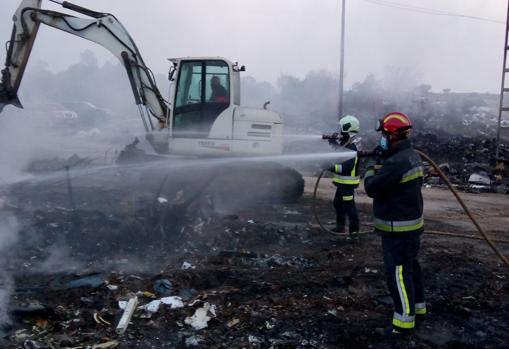 Dos bomberos y una maquinista trabajan esta tarde para refrescar una zona quemada