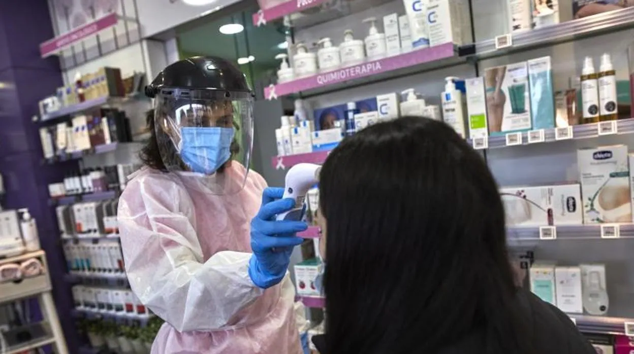 Una farmacéutica toma la temperatura a una mujer antes de realizarle un test de antígenos