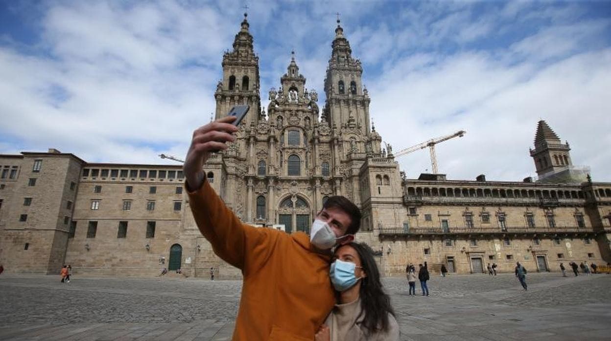 Una pareja se fotografía con mascarillas para protegerse del coronavirus ante la Catedral de Santiago, ya sin andamios