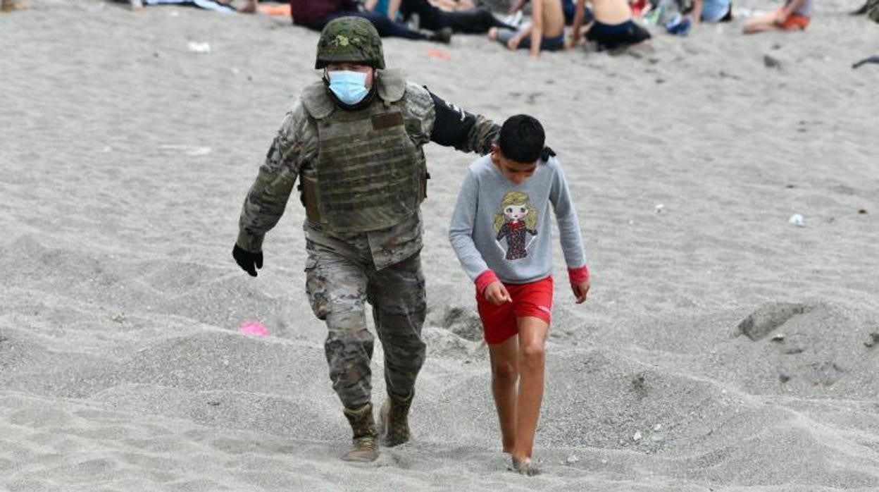 Un niño llega a las playas de Ceuta, acompañado por un miembro del Ejército