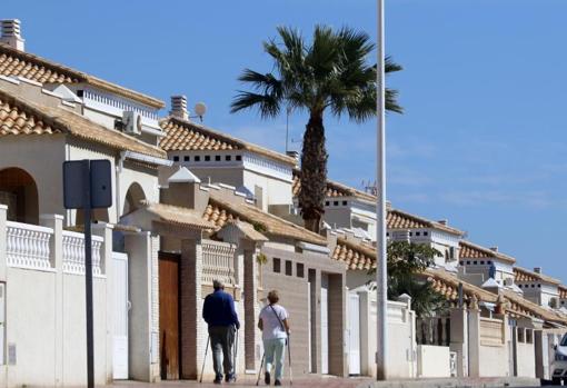 Una pareja de jubilados pasea junto a los bunbalós de una urbanización en Torrevieja