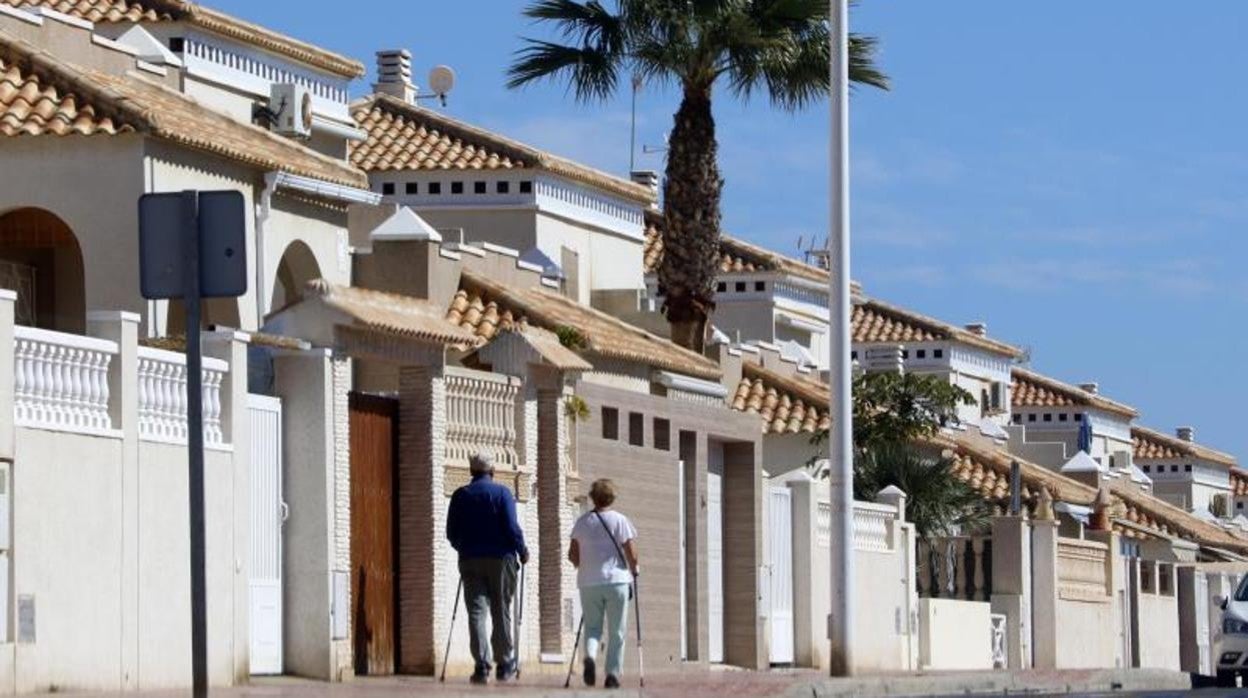 Una pareja de jubilados pasea junto a los bunbalós de una urbanización en Torrevieja