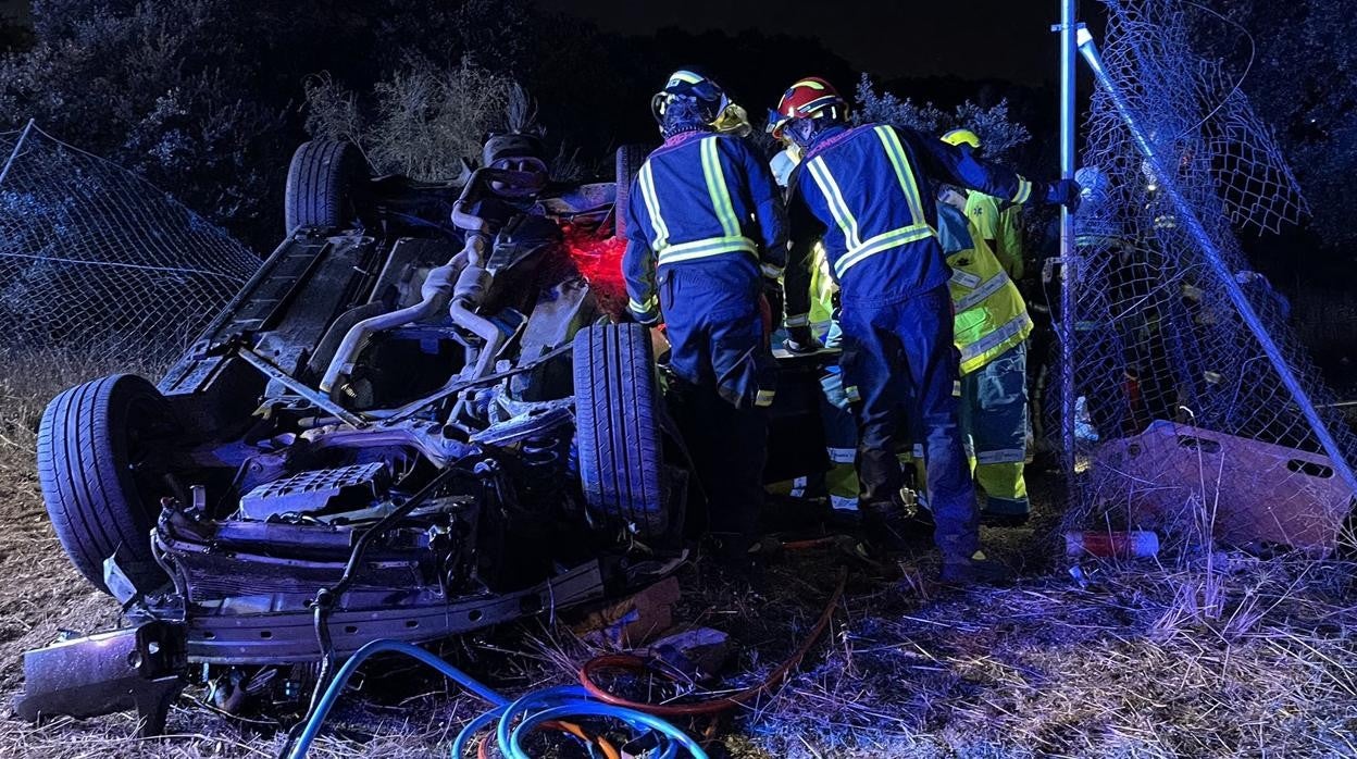 Los bomberos, junto al vehículo siniestrado tras salirse de la vía