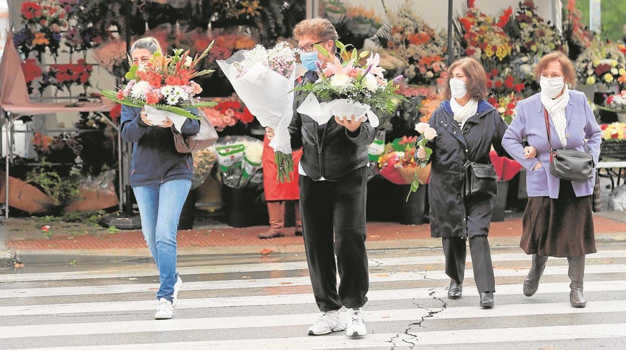 Tres personas llevan flores al cementerio en una festividad anterior