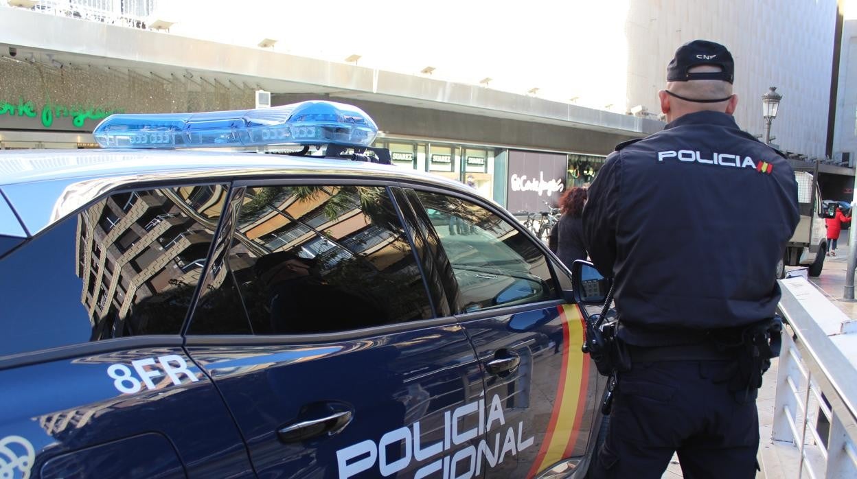 Imagen de recurso de un agente de la Policía Nacional junto a su coche patrulla en el centro de Valencia