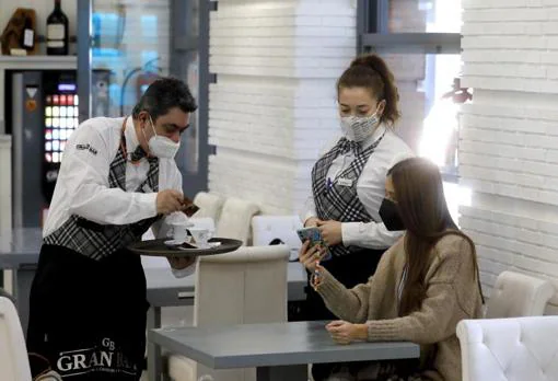 Una joven muestra su pasaporte covid en una cafetería