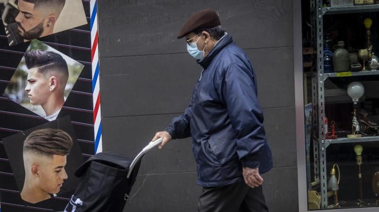 Un hombre con mascarilla empuja un carro por una calle de Alicante