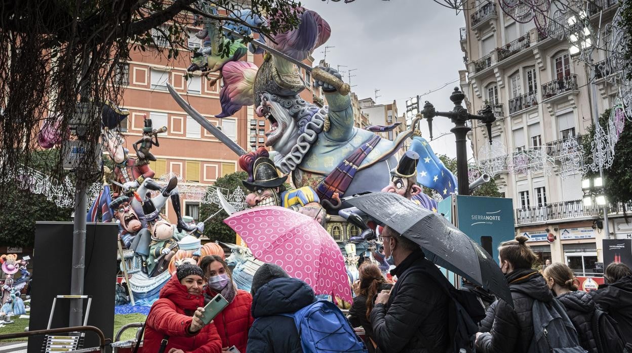 Imagen de personas con paraguas por la lluvia contemplando una falla en Valencia