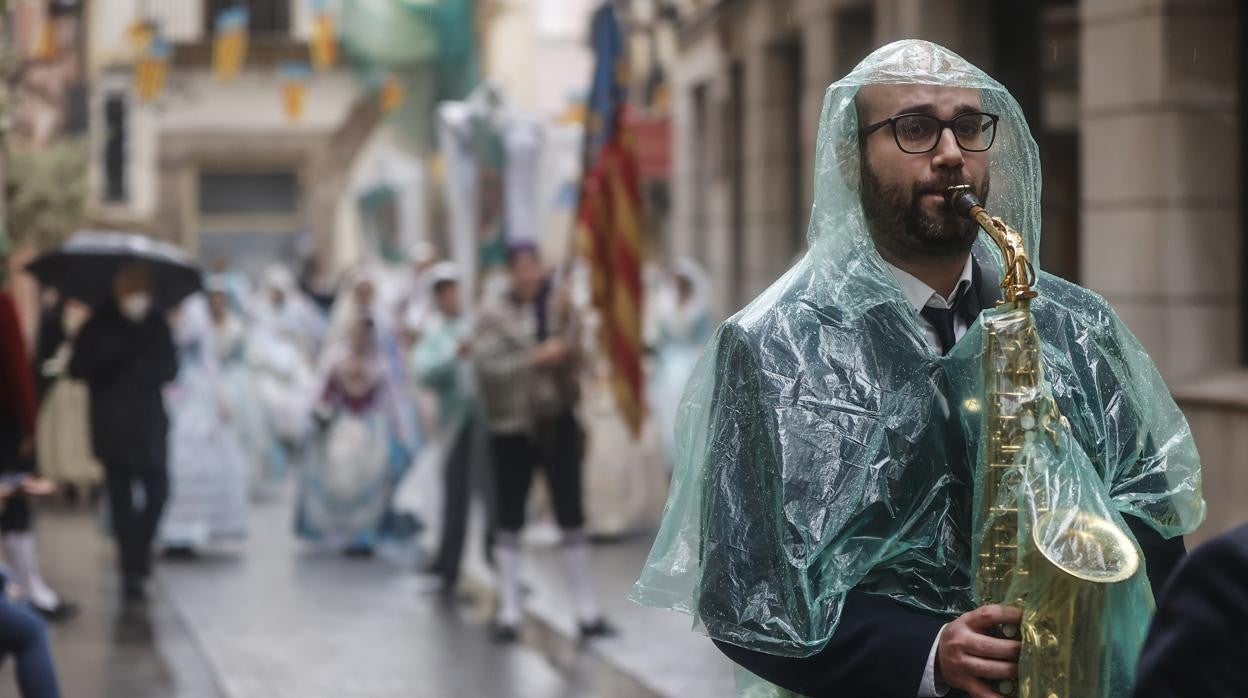 Imagen de un músico desfilando con un chubasquero por la lluvia en Valencia