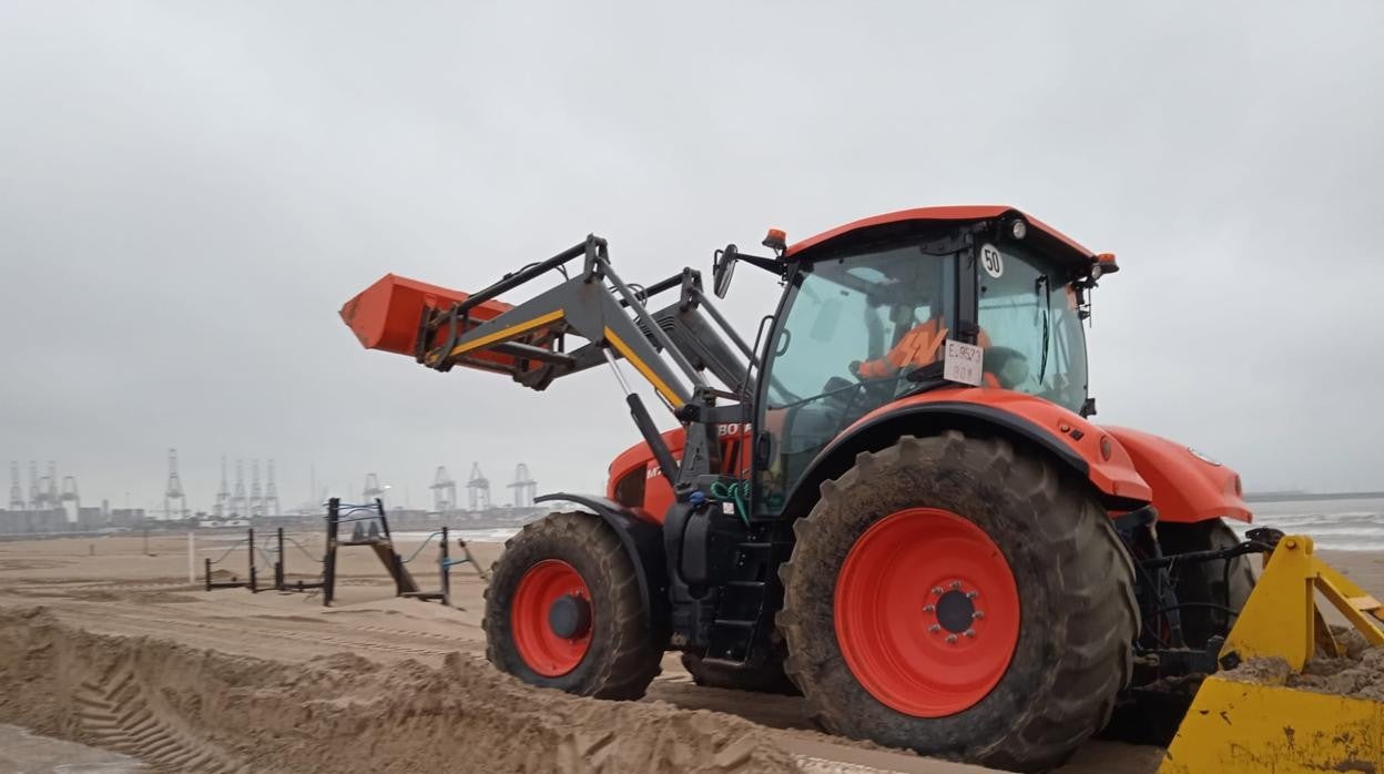 Un tractor trabaja en las tareas de arrastre de la arena en una playa de Valencia