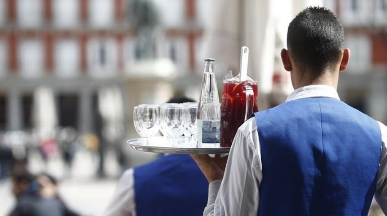 Un camarero lleva bebidas a una mesa en foto de archivo