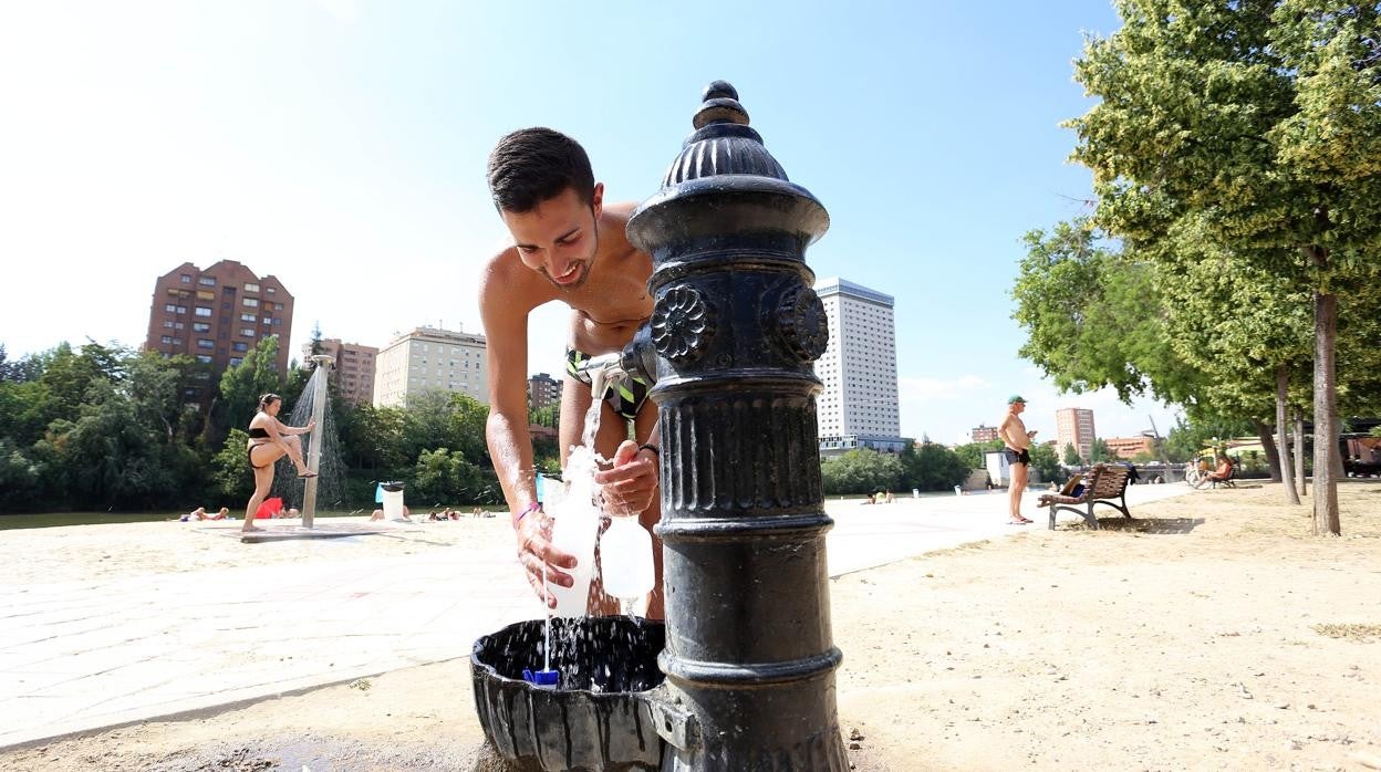 Un vallisoletano recoge agua de una fuente en la playa de las Moreras, en Valladolid