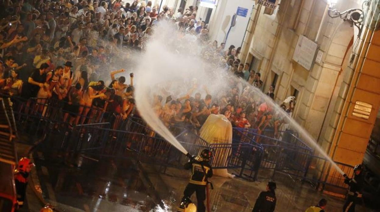 Los bomberos dirigen sus mangueras hacia al público en la tradicional banyà alicantina