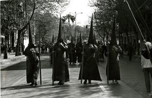 Estación de penitencia de 1983, con ocho nazarenos portando cirios apagados y...