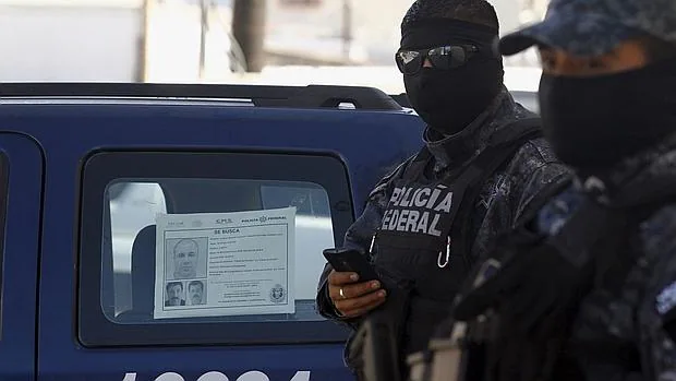 Miembros de la Policía Federal j unto a un vehículo en el que se puede ver un cartel de busca y captura contra «El Chapo»