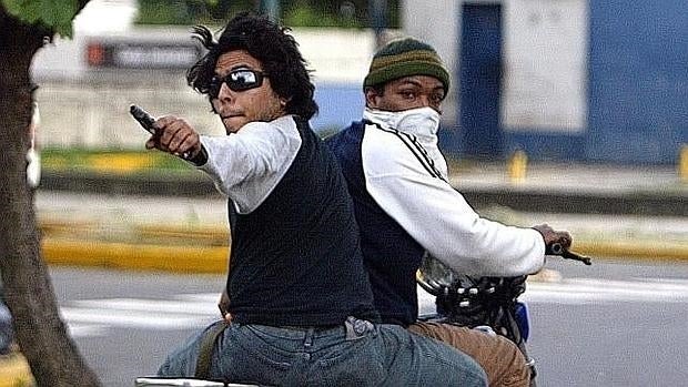 Dos chavistas apuntan con un arma a opositores, durante enfrentamientos en un campus universitario, en Caracas