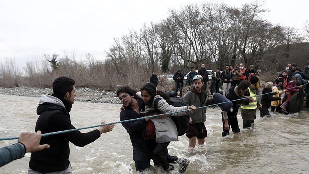 Un grupo de refugiados cruza el río que separa la frontera de Macedonia y Grecia